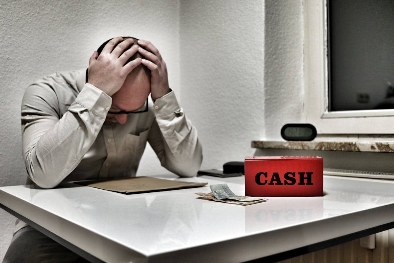 Stressed person holding head with cash box on desk